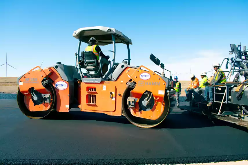 An L.A. Fuller and Sons crew paves an asphalt road with a VÖGELE SUPER 2003-3i paver and compacts it with HAMM smooth drum rollers. 