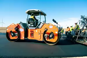 An L.A. Fuller and Sons crew paves an asphalt road with a VÖGELE SUPER 2003-3i paver and compacts it with HAMM smooth drum rollers. 